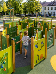 Nowoczesny labirynt dla dzieci na dużym placu zabaw w parku miejskim. Drewniane i kolorowe przejścia, dzieci bawiące się naturalnie,